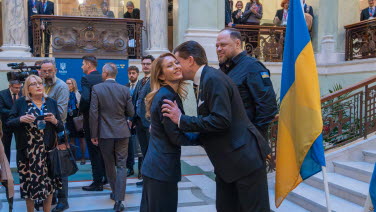 One of the two Speakers greeting a woman Speaker with a hug.