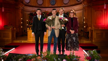 Fyra personer står framme vid podiet i Andrakammarsalen.