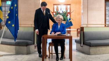 En person signerar gästboken och en person står över hennes axel och tittar 