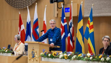 En man står i talarstolen med flaggor i bakgrunden.