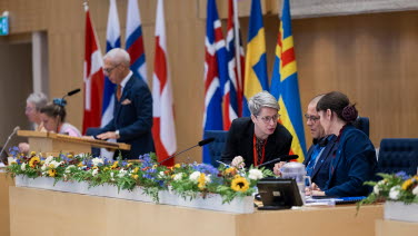 Deltagare vid talmanspodiet talar med varandra, till synes med låg ton.