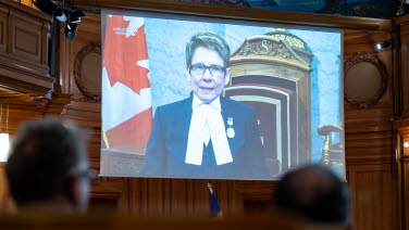 4 A woman speaks via a big screen in the former Second Chamber. The image shows the Canadian flag.