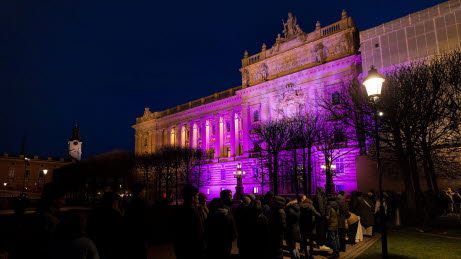 Östra riksdagshuset upplyst med en lång ringlade kö utanför.