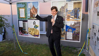 Talmannen står framför en affischutställning i ett tält.