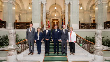 Fem personer står uppställda för gruppfoto i riksdagens trapphall.