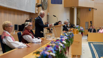 Kungen står i kammarens talarstol. Bortom honom syns talman Andreas Norlén och i förgrunden syns tredje vice talman Kerstin Lundgren och andre vice talman Julia Kronlid.
