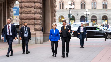 Två personer går jämte varandra på Riksgatan. Säkerhetsvakter håller sig i närheten.