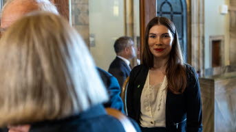 En kvinna i långt mörkt hår ler mot kameran. I förgrunden syns en kvinna i page.