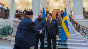 The two Speakers shake hands with a person wearing a hat.