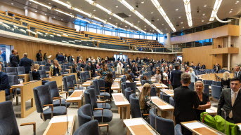 Riksdagens kammare sedd från sidan. Personer är på väg till sina platser.