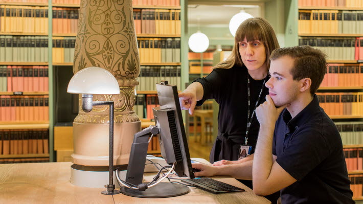 Bibliotekarie Anna Nyströmer hjälper en student att söka i bibliotekets digitala tjänster. De står framför en dator, Anna pekar på skärmen.