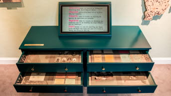 En grön sekretär med utdragna lådor och en skärm som visar gamla klipp och flygblad.