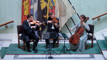 Tre musiker som spelar violin, viola resp. cello spelar med en trappa i bakgrunden.