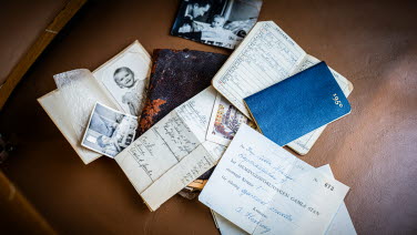 Foton, anteckningar och kalendrar ligger utspridda på ett bord. I mitten syns en nött plånbok i läder.