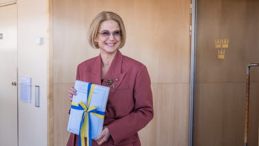 Finansministern står med den tryckta budgeten i famnen. Hon ser glad ut.