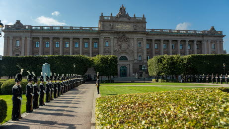 Östra riksdagshuset. I förgrunden syns Riksplan där uniformsklädda personer står uppradade.
