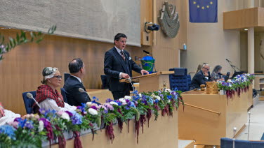 Talman Andreas Norlén står i talarstolen i kammaren. Till vänster två vice talmän