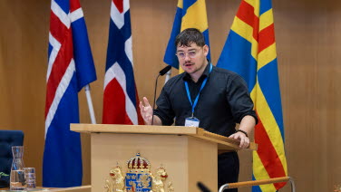 Ung man står i talarstolen med nordiska flaggor i bakgrunden,