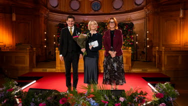 Tre personer står framme vid podiet i Andrakammarsalen.