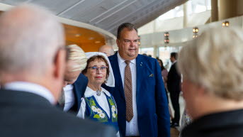 En kvinna i folkdräkt med prästkragar på västen samt en man i blå kavaj och brun slips.