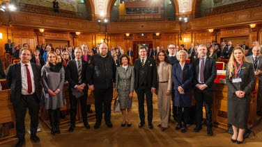 Group photo of 13 people in the former Second Chamber.