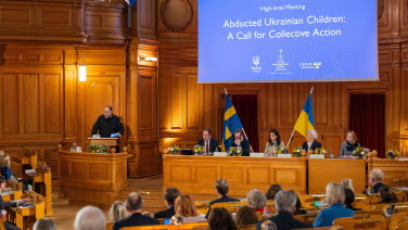 A man stands at the rostrum. Panellists sit on the platform.