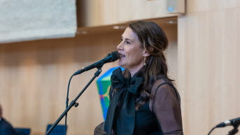 En kvinna i långt mörkt hår står vid en mikrofon. 