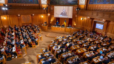The former Second Chamber is full. Photo taken from the gallery. A woman Speaker stands at the rostrum.