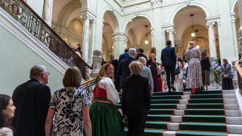 En ström med festklädda människor går upp för en trappa. Pelare och valv syns i bakgrunden.