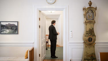 Talman Andreas Norlén inväntar partiledarna. Till höger en gammal golvklocka.