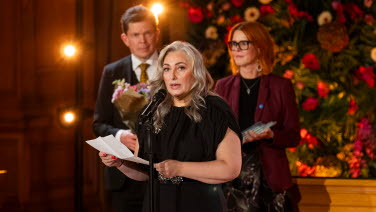 Tre personer står framme vid podiet i Andrakammarsalen.