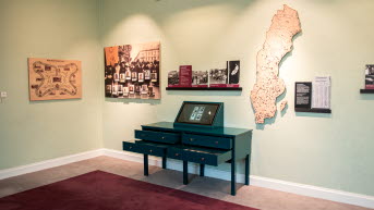 Ett hörn med kort på väggen, en sverigekarta och en sekretär med utdragna lådor