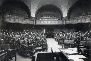 Svartvit bild på riksdagens Förstakammarsal. Ledamöterna syns framifrån.