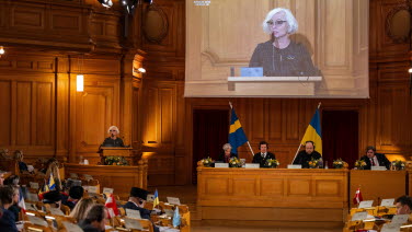 Woman gives an address in the former Second Chamber. She can be seen on the big screen.