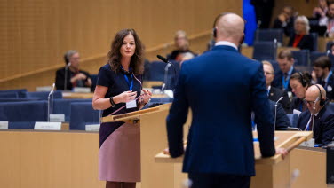 En kvinna står i talarstolen och debatterar med en man som har ryggen mot kameran.