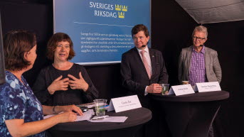 Fyra personer står i en panel framför en storskärm.
