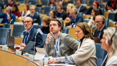 Delegater sitter i sina bänkar och lyssnar.