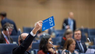 Person håller upp en skylt med siffrorna 057 i kammaren.