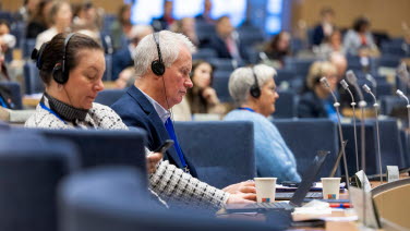 En man och en kvinna sitter i sina bänkar och lyssnar.