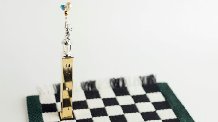 Silverstaty står på ett vävt schackbräde.