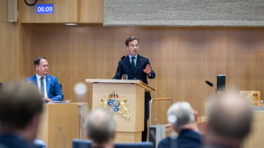 Statsministern står i talarstolen. Till vänster förste vice talman. I förgrunden sitter riksdagsledamöter och lyssnar.
